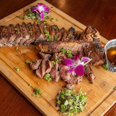Grilled steak on a wooden board garnished with herbs and purple orchids.