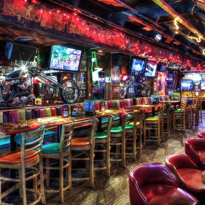 A vibrant bar with colorful stools and booths, neon lights, and motorcycles displayed on the bar
