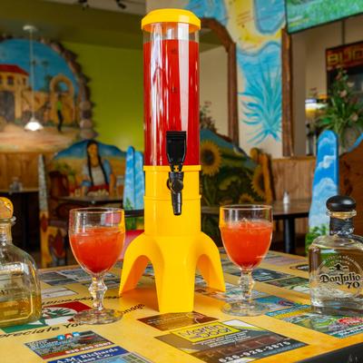 A dispenser filled with a red beverage, flanked by two tequila bottles and glasses.