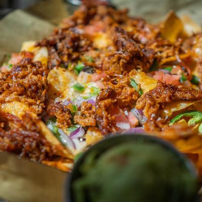 Nachos topped with jalapenos, tomatoes, black onions, peppers, melted cheese, closeup