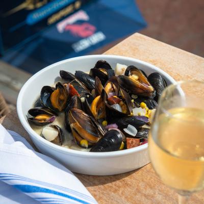 Bowl of mussels served on the table with a glass of white wine.