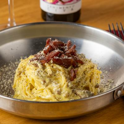 Pasta carbonara topped with guanciale and grated cheese.