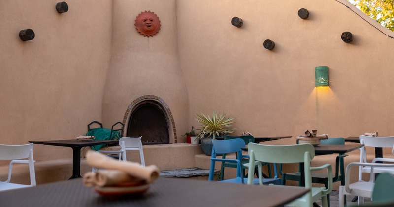 Outdoor patio with adobe-style walls, a kiva fireplace, and colorful chairs