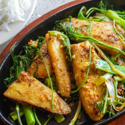 Dish served in a skillet featuring white fish marinated in turmeric and galangal.