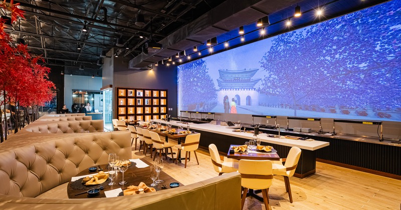 Upscale interior with banquette seating, red-leafed trees and a large digital screen