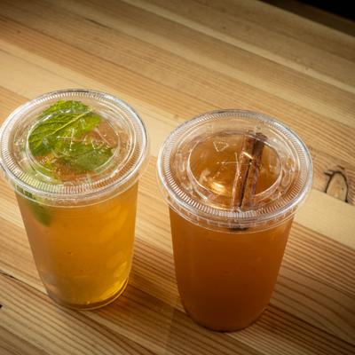 Two clear plastic cups filled with iced tea, garnished with mint and a cinnamon stick.