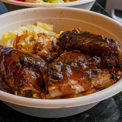 A bowl of three pieces of glazed, dark brown chicken legs with cabbage.