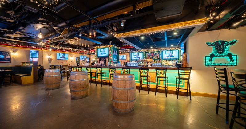 Stylish and cozy interior of a sports bar with a large bar and wooden barrels as standing tables