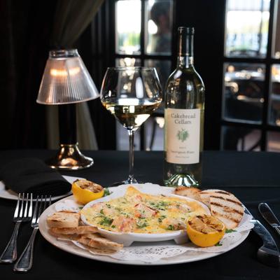 Lobster Cargot plate, white wine and a lit lamp on a black tablecloth.