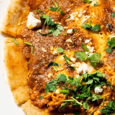 Shakshuka toppd with cheese crumbles and herbs, close-up.