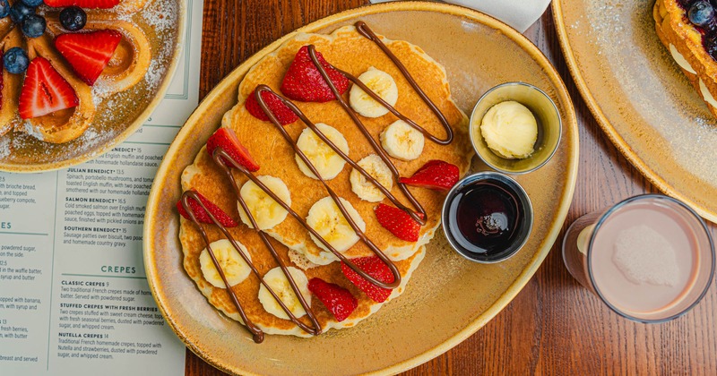 Pancakes topped with banana slices, strawberries, and chocolate drizzle