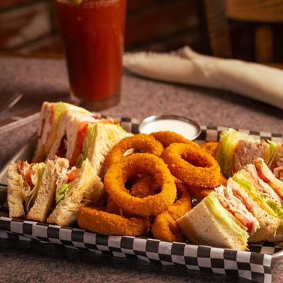Turkey Club Sandwich served with onion rings, accompanied with a glass of Bloody Mary.