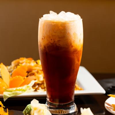 Thai iced tea served in tall glass, alongside food.