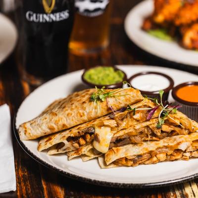 Sliced chicken quesadilla served with guacamole, sour cream, and salsa.