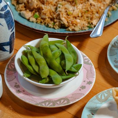 Edamame in white bowl on patterned saucer, accompanied with other dishes.