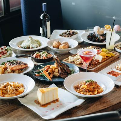 Assortment of food items served on the table alongside cocktails and a bottle of wine.