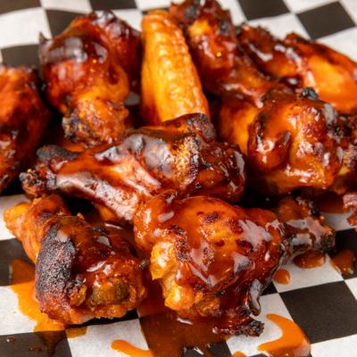 BBQ chicken wings with sauce on a checkered paper-lined tray.