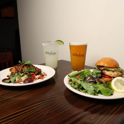 plate of Grilled salmon and plate of Grilled Chicken sandwich with house salad , Beer and margarita.
