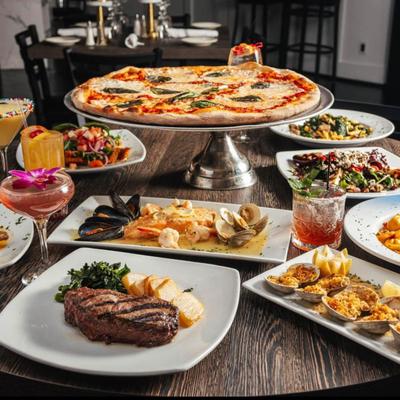 A large pizza on a stand, steak, seafood, salads and other food plates, and colorful cocktails.