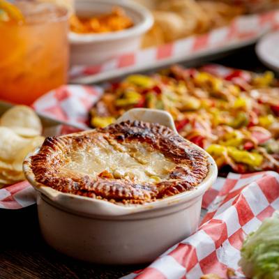 Chicken pot pie served alongside a whole pizza, chips and a iced drink.