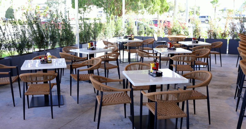 Outdoor cafe area with white square tables, rattan chairs, and condiment caddies