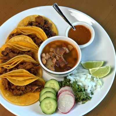 Marinated pork tacos, served with soup, cucumber, radish, onion, cilantro, lime, and salsa.