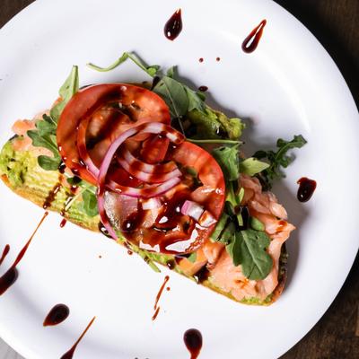Avocado salmon toast topped with tomatoes, arugula, onion and balsamic glaze.