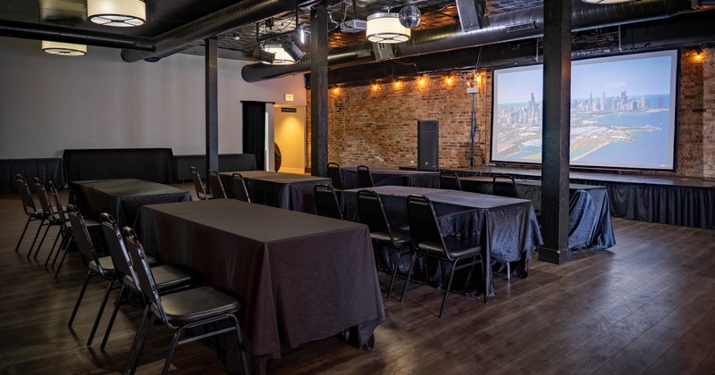 Event space with black tables, chairs, and a large projector screen
