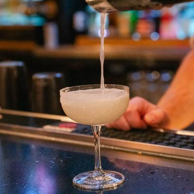 A bartender pouring a cocktail into a glass on bar counter.