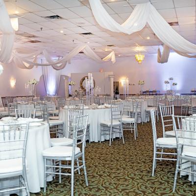 Wedding banquet hall with round tables, silver chairs, and floral centerpieces.