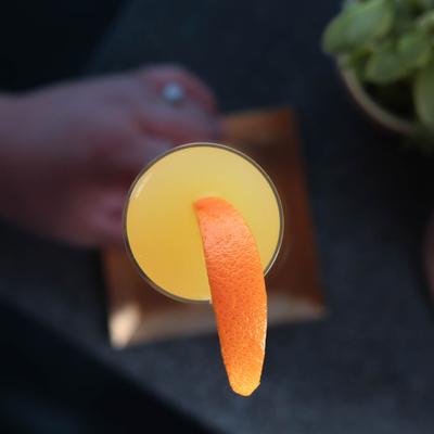 A top-down view of a yellow cocktail garnished with an orange slice.