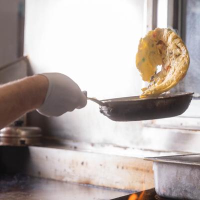 A hand in a glove flipping an omelet from a frying pan over open flames.