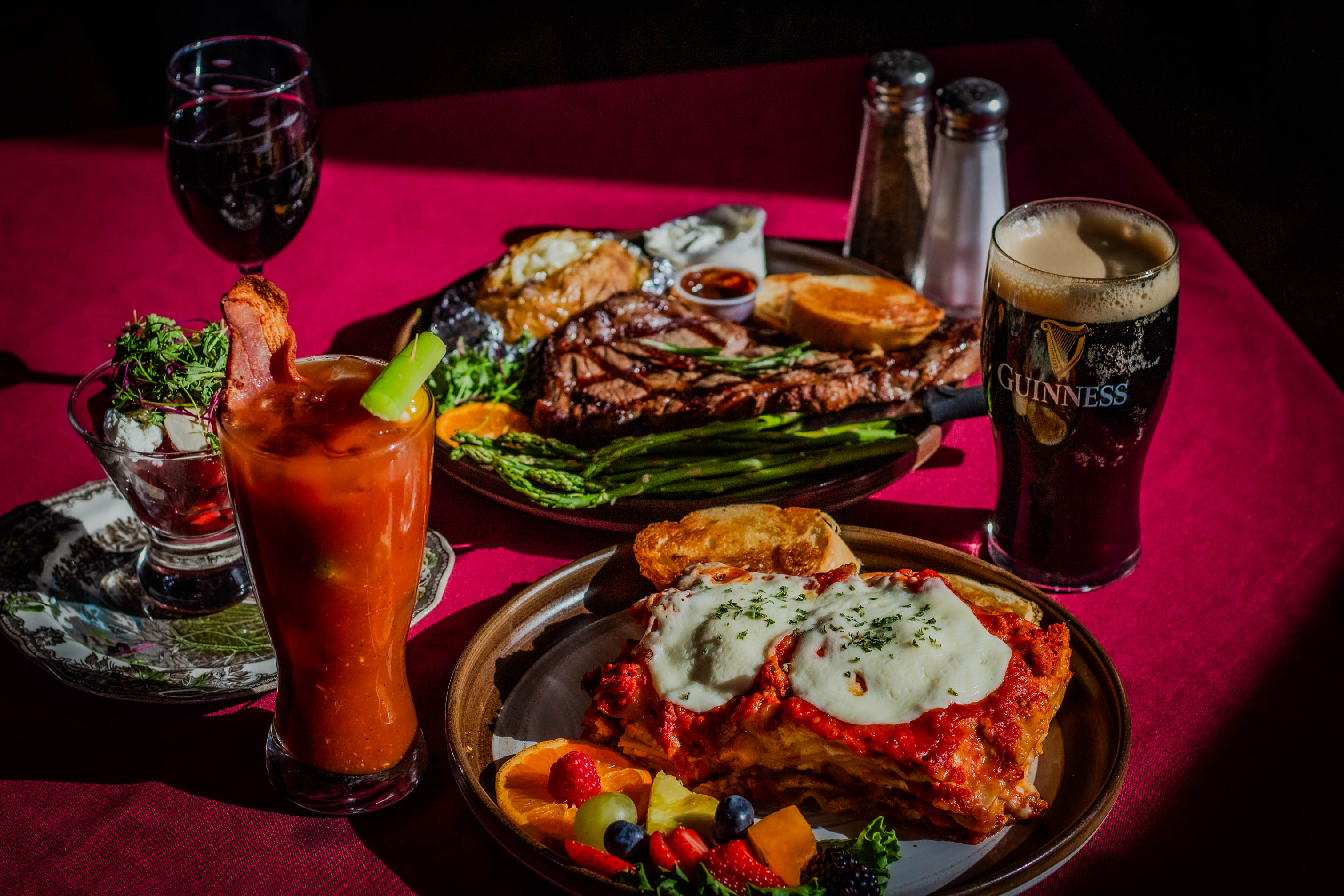 Plates of lasagna and steak with sides served with drinks on a table