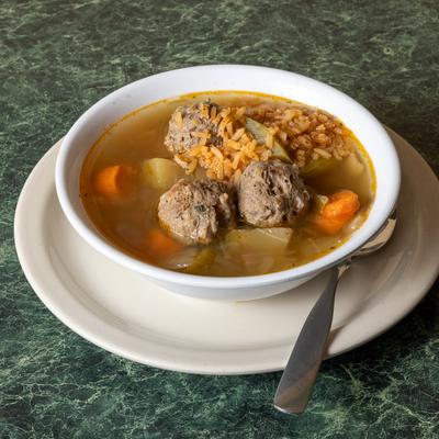 Bowl of hearty meatball soup with vegetables and rice on a green granite table.