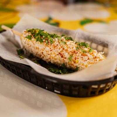 Mexican street corn on a stick, topped with cream, cheese, and chili.