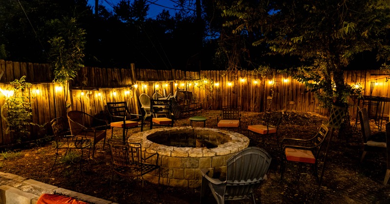 Alt-text: An outdoor gathering space at night with a circular stone fire pit surrounded by chairs