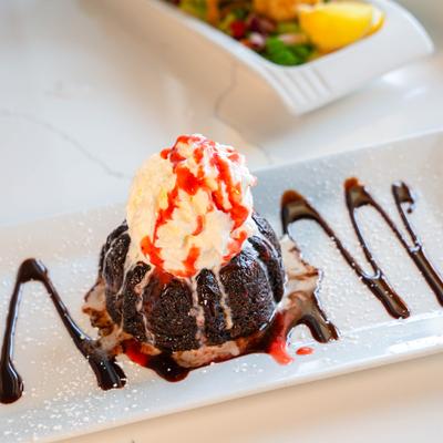 Chocolate lava cake with whipped cream, strawberry sauce, and chocolate drizzle.