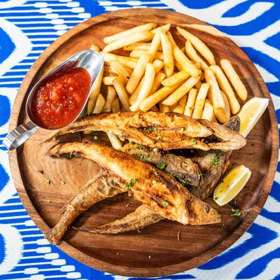 Fried fish with fries and tomato sauce served on a wooden platter.