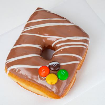 A square-shaped chocolate donut with white icing and colorful M and M candies.