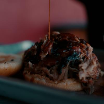 Open pulled pork sandwich being topped with barbeque sauce, close-up.