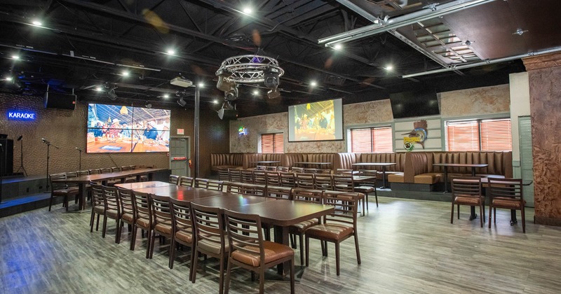 Interior of a restaurant with wooden tables and chairs, booth seating, and large display screens.