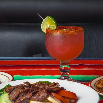 Spicy red cocktail with chili rim and lime served next to a steak dinner.