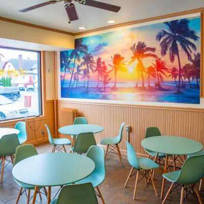 Colorful cafe interior with a tropical sunset mural and mint green tables.