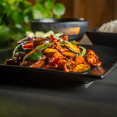 Basil chicken with vegetables served on a black rectangular plate.