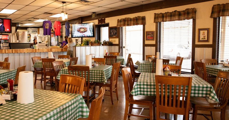 Interior, dining area, tables for four ready for guests, bar in the back, wooden chairs