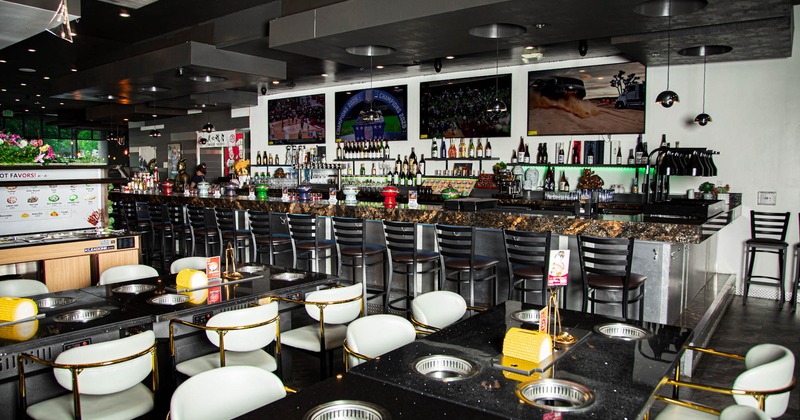 Interior of a modern restaurant with grill tables and a long bar counter