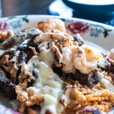 Grilled chicken, steak, and shrimp covered in cheese sauce, served over rice.