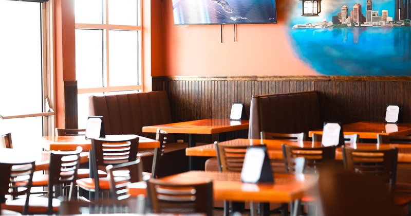 Interior with orange tables, brown chairs, a TV showing a coastline, and a cityscape mural