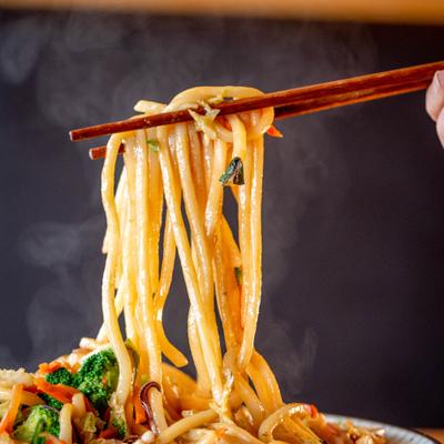 Noodles lifted with chopsticks above a steaming bowl.