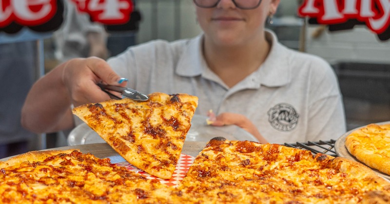 An employee serves a slice of pizza from a large chicken pie
